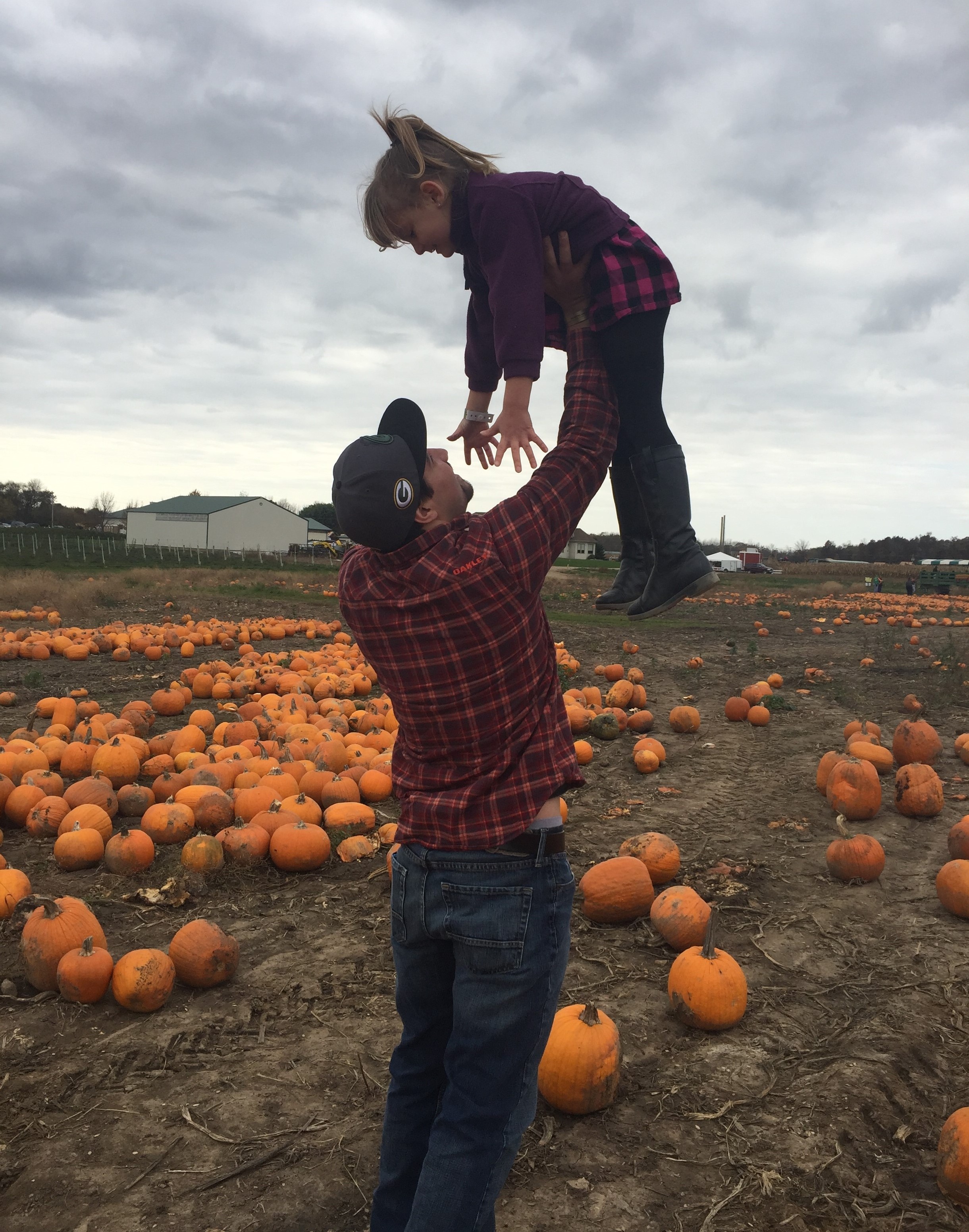 Daniel holding Emma above the pumpkin patch